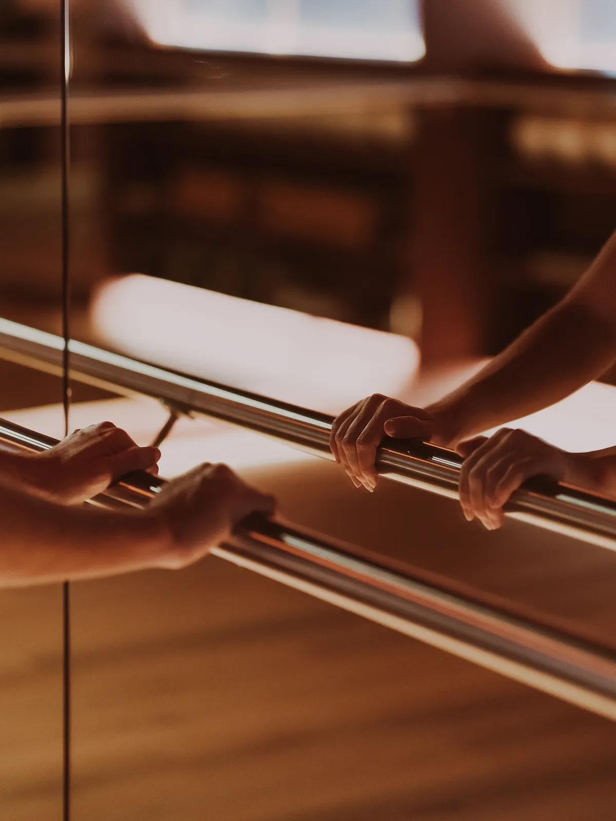 Deux mains posées sur la barre, reflétées dans le miroir du studio