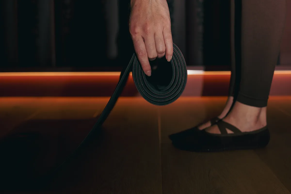 Main tenant un tapis roulé au bord de la salle, avant un cours de Pilates Mat