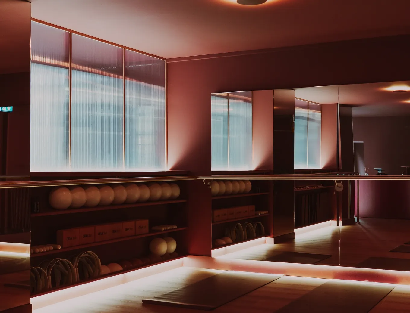 Salle principale du studio : verrière cannelée, miroirs et étagères de ballons de Pilates