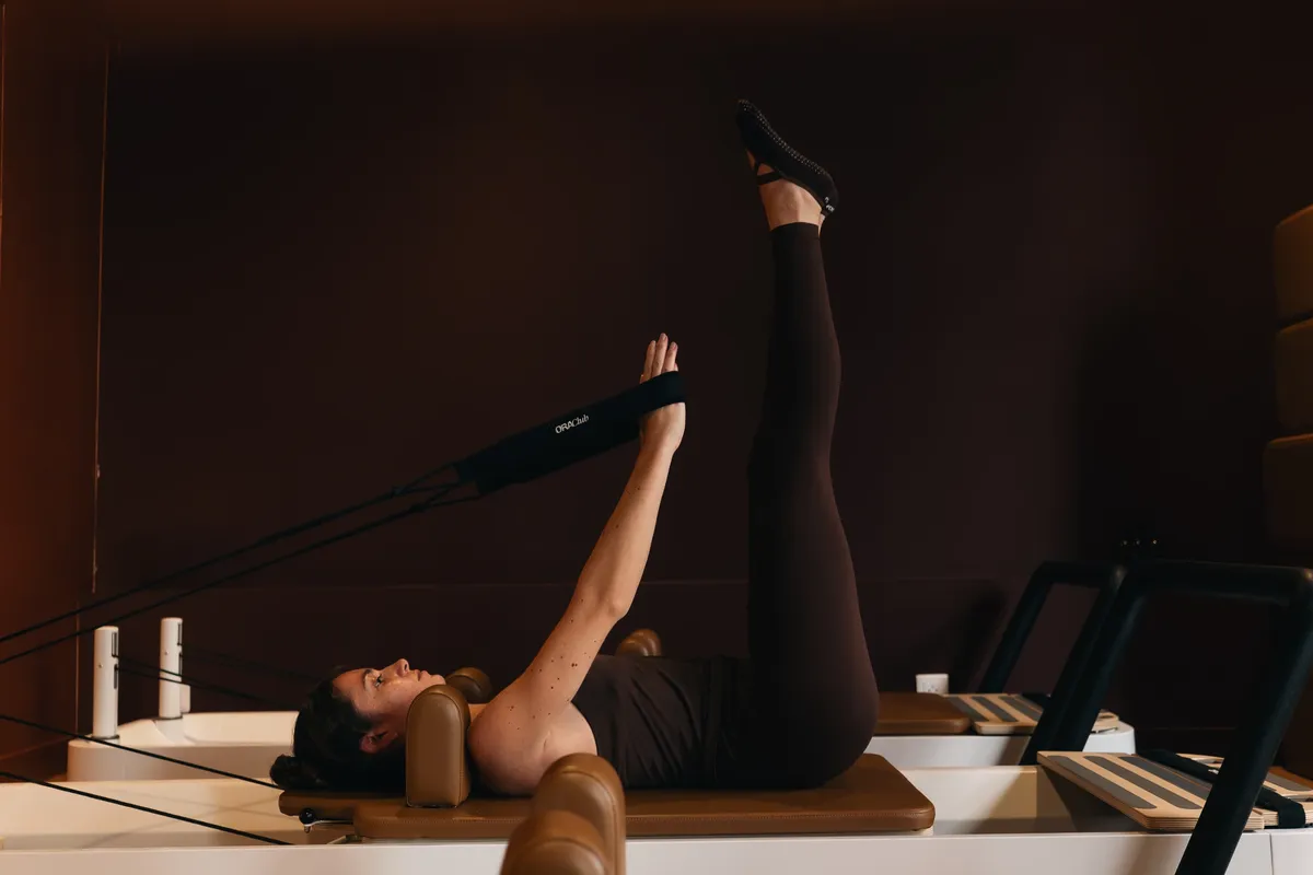 Pratiquante allongée sur le Reformer, jambes tendues, tirant les sangles Ora Club
